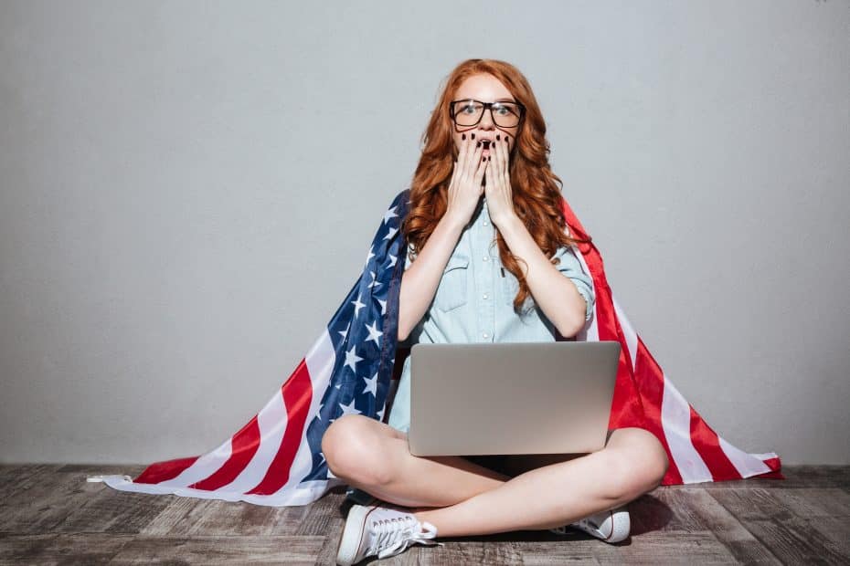 Mulher ruiva assustada, com a bandeira dos Estados Unidos nas costas e um notebook no colo