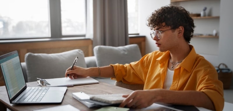 Homem tomando notas diante de notebook aberto