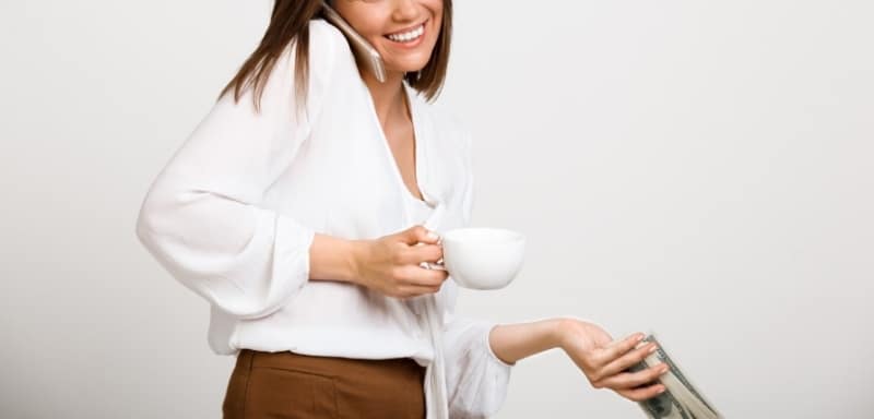 Mulher ao telefone, com uma xícara na mão e um montinho de dinheiro na outra